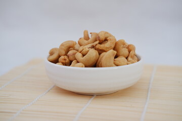 Roasted cashew nuts in white bowl on bamboo mat, stock photo