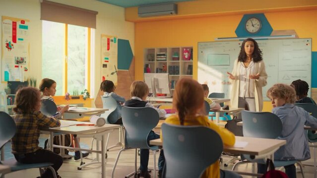 Caring Teacher Explaining a Math Lesson to a Classroom Full of Bright Diverse Children. Little Girl Raising Her Hand and Asking Tutor a Question. Primary School with a Group of Smart Multiethnic Kids