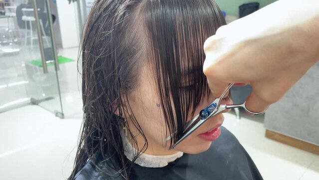 Caucasian female hairdresser working in hair beauty salon, cutting hair of caucasian woman. The hairdresser cuts her bangs, slow motion. Health and hygiene in workplace