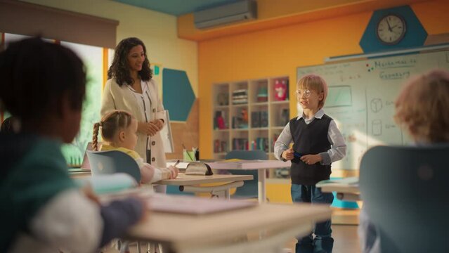 Elementary School Mathematics and Geometry Class: Portrait of a Cute Boy in Glasses Showcasing His Multiplication Table Knowledge in Front a Classroom Full of Classmates and a Happy Young Teacher