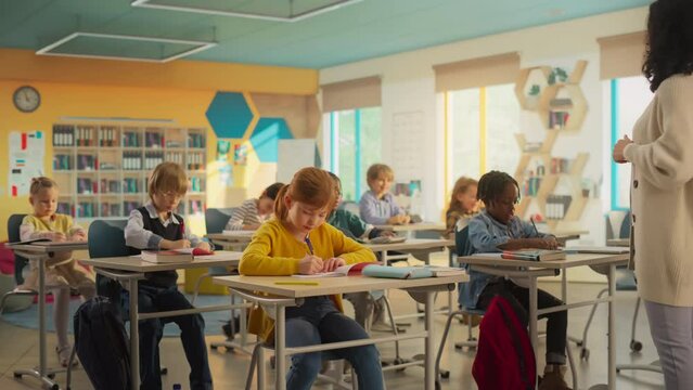 Class of Adorable Multiethnic Children Listening to a Lecture from a Teacher and Writing Down Notes in an International Elementary School. Enthusiastic Female Explains New Subjects to Young Smart Kids