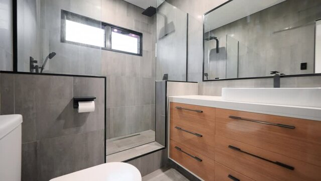 Executive double shower with modern wooden cabinetry grey floor to ceiling tiles and full length mirror restroom interior.