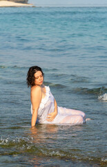 Fototapeta na wymiar Beautiful woman in white dress sits in the water on ocean shores