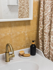 Minimalism is the style of the bathroom interior with yellow ceramic tiles on the wall - a mirror, a sink with a dispenser and soap, a brass faucet, a shower curtain. Mediterranean style