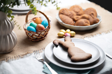 Gingerbread cookie shaped as Easter bunny on gray plate at festive decorated table. Holiday...