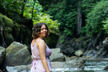 A young woman in beautiful pink dress poses on the banks of the river and  rainforest.