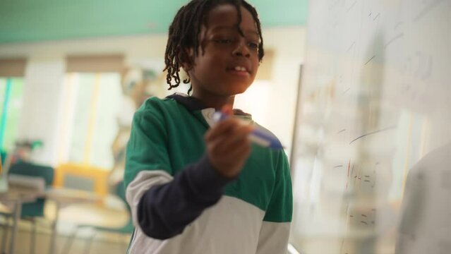 Talented Small Boy Solving an Arithmetic Equation. Portrait of a Happy Elementary African American Pupil Studying Hard, Writing Numbers on a Whiteboard During a Math Class