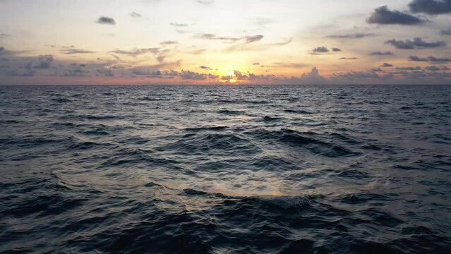 Flying over the ocean waves during sunset as the sun disappears into night. bird eye view 4K cinematic drone footage.