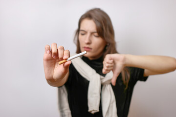 Fototapeta premium The girl holds a cigarette in her hand and points her finger down. The concept of the bad habit of smoking.