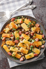 Fried potato dumplings with bacon, onions and mushrooms close-up in a plate on the table. Vertical top view from above