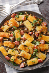 Polish fried potato dumplings Kopytka with bacon, onions and mushrooms close-up in a plate on the table. Vertical top view from above