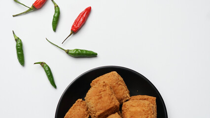 Fried tofu on a black plate with chilies in a white background