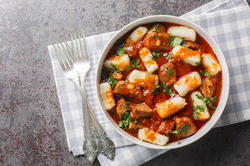 Kopytka Polish dumplings or little hooves made of mashed potatoes served with meat with gravy close-up in a plate on the table. Horizontal top view from above