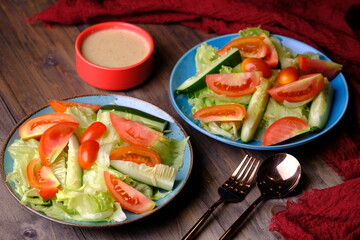 fresh raw vegetable salad. iceberg lettuce, sliced tomatoes, sliced cucumber and cherry tomatoes with peanut sauce salad dressing.