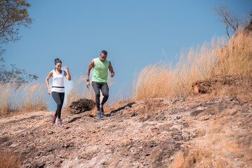 Young Ethnicity African American couple running trail outdoor activities at mountain in Autumn season, happy woman and man wearing sport wear spend time together jogging or training in sunny day