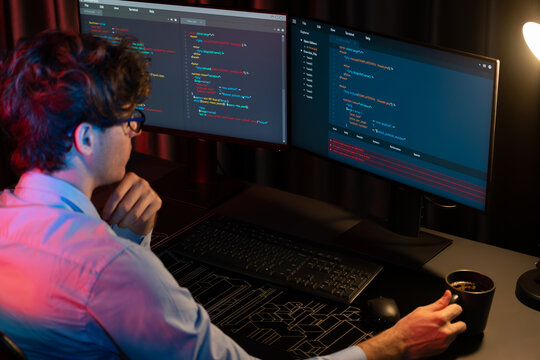 Working IT developer concentrating online software while drinking coffee on surrounded by coding application pc screens, creating program for firmware on website at neon modern office home. Gusher.