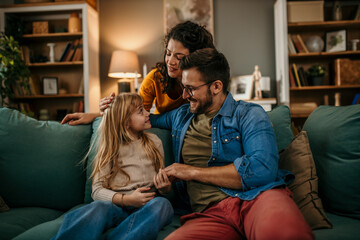 Parents and their daughter sharing laughter and conversation on the living room sofa