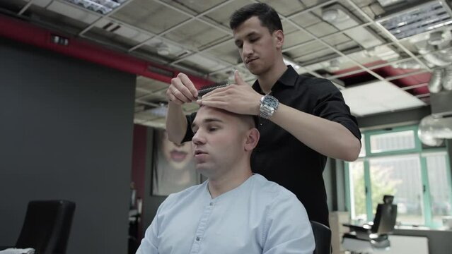 A handsome male hairdresser combs the hair of a young caucasian male client with a comb after a haircut. Professional fashionable haircut in a barbershop. Slow motion