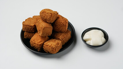 Fried tofu on a black plate with mayonnaise on a white background