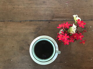 cup of hot black coffee with red and white flowers, putting on an antique wooden table