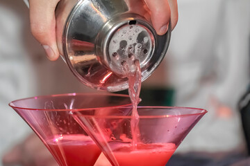 A bartender skillfully crafting a mixed drink, elegantly pouring it into a martini glass.