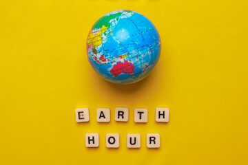 Wooden cubes with words Earth Hour and a globe over yellow background. World earth day and earth hour concept