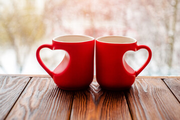 two heart shaped mugs with tea on the background of a window in winter
