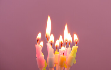 Pastel colored birthday candles burning and melting on pink background. Copy space for text.	