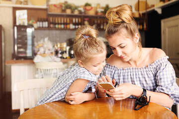  Happy mother and little girl having dinner and using smartphone at restaurant.