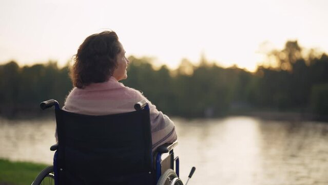Woman in wheelchair walking in city. Senior mature smiling woman breathing air outdoor thinking looking around enjoying pastime in evening. Live with physical disability, special needs people concept.