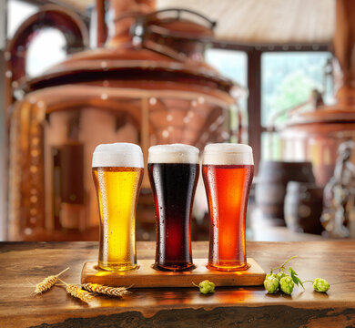 Set of glasses of different beer on wooden table and blurred copper brewing system at the background.