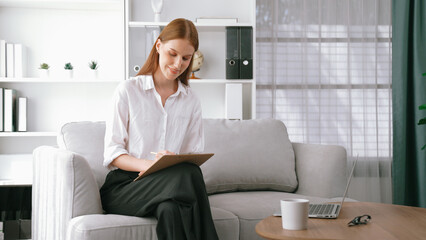 Professional female psychologist with clipboard portrait sitting on arm chair in psychiatrist...