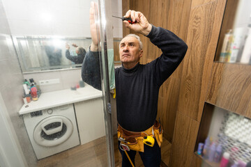 man repairs the shower door in the bathroom. A male repairman repairs the shower cabin.