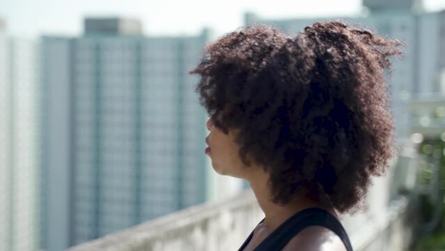 Young African American woman in afro hairstyle looking far distance into the skyline buildings at rooftops. Female athelete determined in sport outfit - 4K Real time Footage
