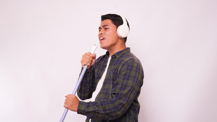 Asian man listening music with headphone and singing on broom
