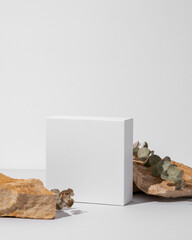 White empty box on texture stones with eucalyptus on light background with shadow.
