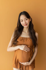 Portrait of beautiful asian young pregnant woman touching belly standing on colour background