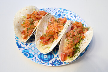 tacos with salmon and tomato on a blue plate on a white background
