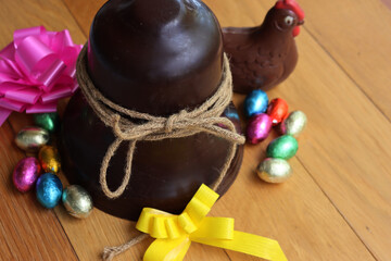 Easter chocolate bell with chocolate eggs, chocolate chicken  and pink and yellow bows on a wooden...