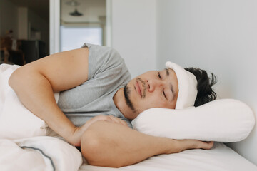 Side view of Asian man getting sick with white towel on forehead, bad symptom, resting and lying on white bed alone in apartment.