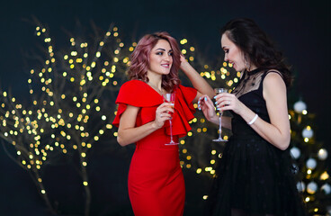 Smiling women in evening dresses with glasses of champagne over lights background