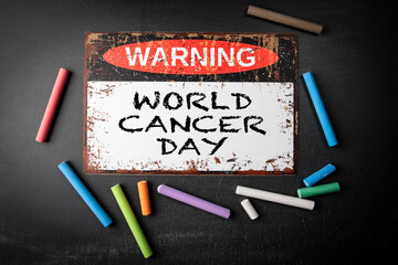 World Cancer Day. 4 February. Metal warning sign and colored pieces of chalk on a dark chalkboard...