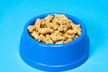A treat for cats and kittens is a fish-shaped catnip cookie in a blue bowl