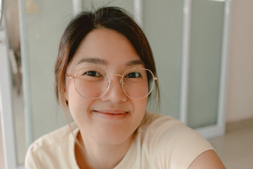 Happy asian Thai woman take selfie and smiling to camera, wearing eyeglasses, relaxing at home.