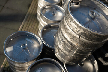 Large damaged 50-liter stainless steel beer barrels are stacked on the terrace of a café. Focus on the barrel on the right