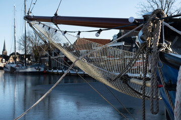 Ship's bow with jib boom and tightly knotted jib net in front of the foremast of a sailing ship. A thin layer of ice on the water in the Dutch village of Lemmer