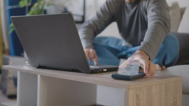Young adult working from home with his pajamas, Uses the living room as an office together with a laptop, He is distracted by a reminder popup from his cell phone that says how to continue today