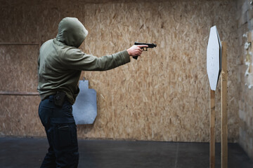 Tactical shooting, a man in a hood shoots with one hand at a ipsc paper target from close distance...