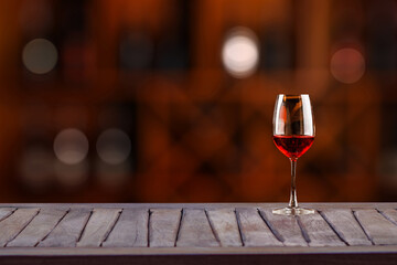 Red wine glass on wooden plank with wine bottle rack as background and blurry wine drinking counter background....