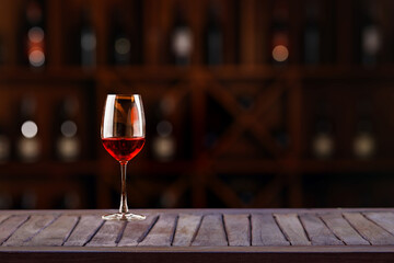 Red wine glass on wooden plank with wine bottle rack as background and blurry wine drinking counter background....
